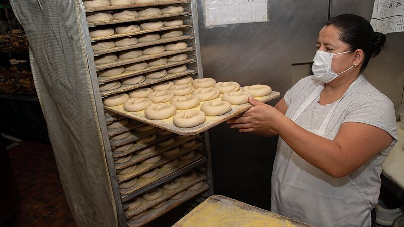 Staff placing uncooked bagels onto a rack
